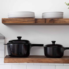 Two black Xtrema ceramic pots with lids on a rustic wooden shelf below white plates.