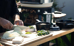 Chef slicing onions on a wooden board next to black Xtrema ceramic cookware.