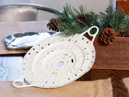 White Xtrema ceramic colander on a burlap cloth with rustic pine cone decorations.