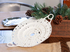 White Xtrema ceramic colander on a burlap cloth with rustic pine cone decorations.