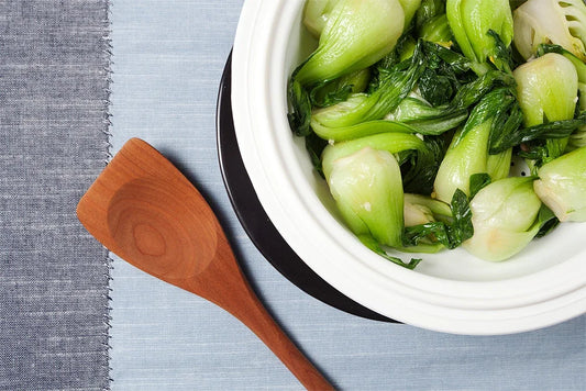 Steamed bok choy in a white Xtrema ceramic pot with a wooden spoon.