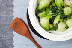 Steamed bok choy in a white Xtrema ceramic pot with a wooden spoon.