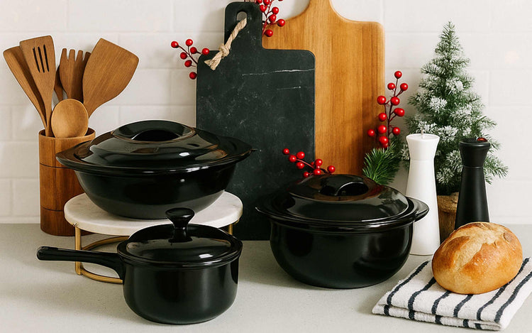 Black cookware set on a kitchen counter with wooden utensils and decorative items.
